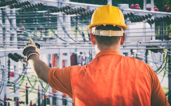 A worker in a hardhat and high-visibility vest working at an electrical plant.